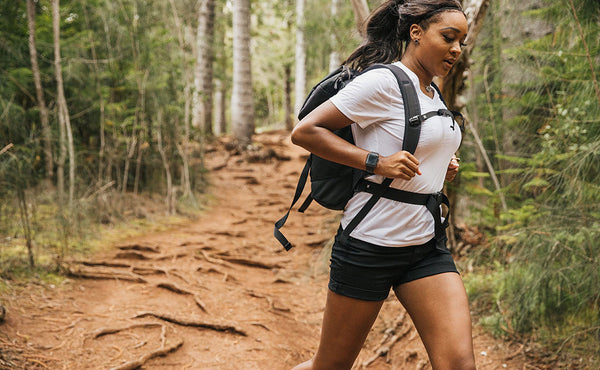 Woman jogging down a hiking trail wearing the Shadow Guide 33 with the sternum and waist belts fastened.